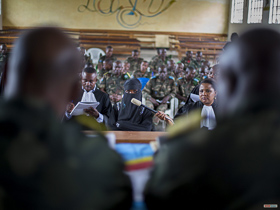  <p class='fr'>
	Une victime, voilée afin de garder l’anonymat, témoigne devant le tribunal militaire pendant une audience à huis clos. Un membre de l’équipe de l’accusation tient le micro et un avocat de la défense prend des notes. Les accusés sont assis au fond de la salle.
	</p> <p class='en'>
	A victim, veiled to protect her identity, testifying before the closed military tribunal. A member of the prosecution team is holding the microphone, and a defense lawyer is taking notes. The accused are at the back.
	</p>
